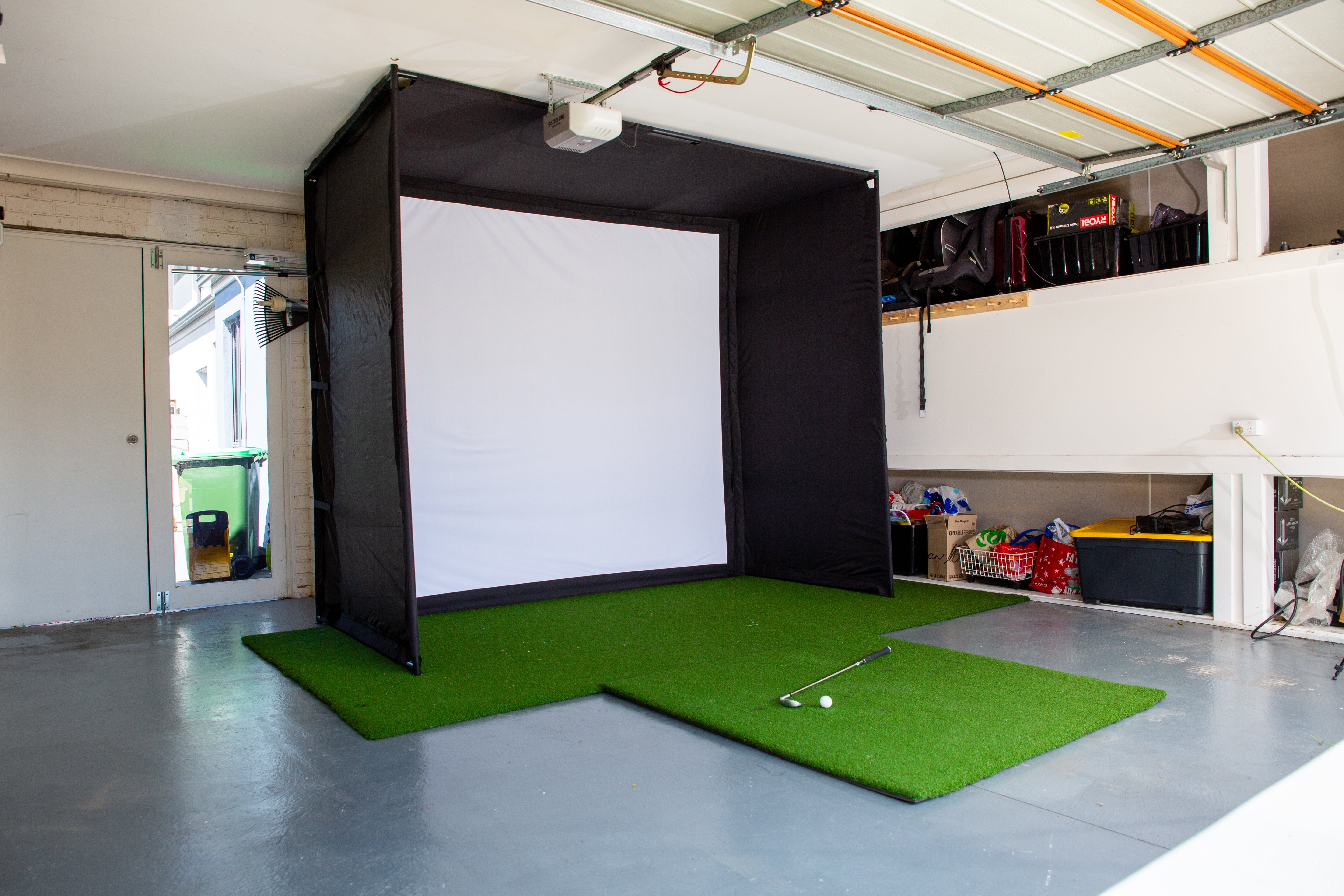 Complete home garage golf simulator setup, featuring a high-impact screen, premium putting and driving turf, and a dedicated hitting mat for a professional-grade indoor training environment.